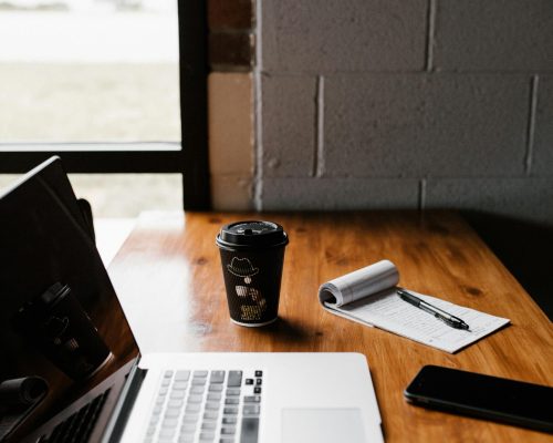 pexels-photo-1967535-1967535 Modern office desk setup with laptop, coffee cup, and notepad by window.